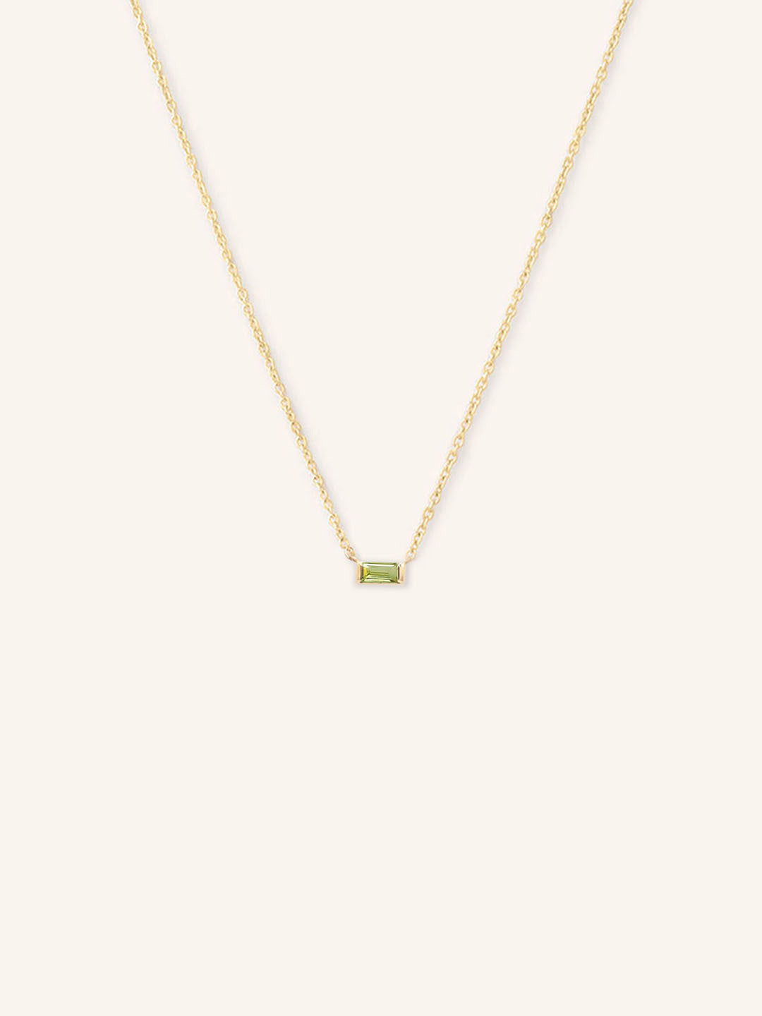 A gold-colored necklace featuring a minimalist baguette design with a peridot gemstone in a white setting.