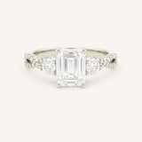 White gold emerald cut three stone diamond engagement ring with pave shoulders on white background
