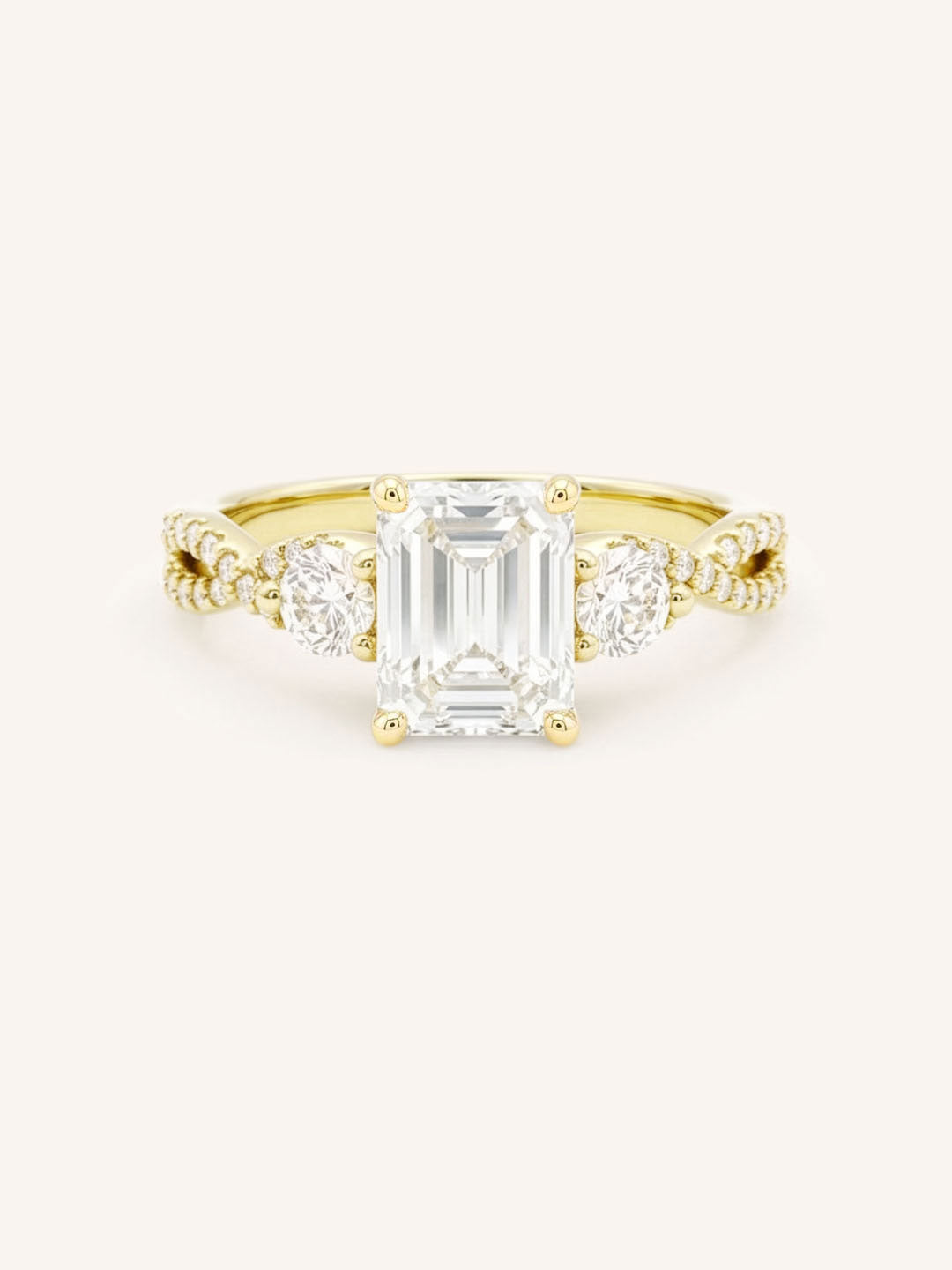 Yellow gold three-stone engagement ring with emerald-cut center diamond and round side diamonds, pave shoulders, on white background