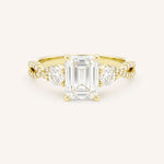 Yellow gold three-stone engagement ring with emerald-cut center diamond and round side diamonds, pave shoulders, on white background