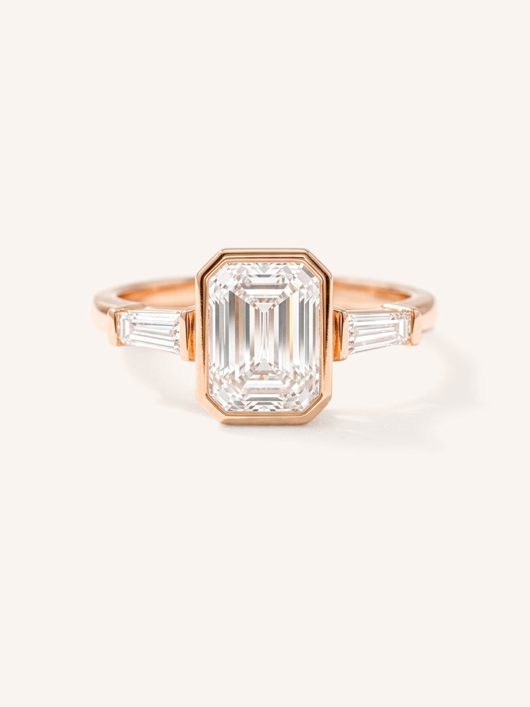Rose gold Grannis emerald cut three stone and baguette diamond engagement ring front view on white background
