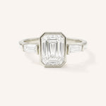 White gold Grannis emerald cut three stone and baguette diamond engagement ring front view on white background