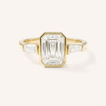 Yellow gold Grannis emerald cut three stone and baguette diamond engagement ring front view on white background