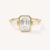 Yellow gold Grannis emerald cut three stone and baguette diamond engagement ring front view on white background