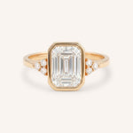 Rose gold emerald cut bezel set diamond engagement ring with side stones on white background