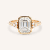 Rose gold emerald cut bezel set diamond engagement ring with side stones on white background