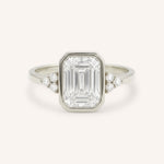 White gold emerald cut bezel set diamond engagement ring with side stones on white background