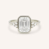 White gold emerald cut bezel set diamond engagement ring with side stones on white background