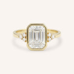 Yellow gold emerald cut bezel set diamond engagement ring with side stones on white background