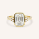 Yellow gold emerald cut bezel set diamond engagement ring with side stones on white background