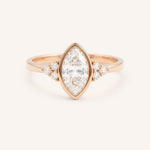 Rose gold marquise cut bezel set diamond engagement ring with side stones on white background