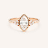 Rose gold marquise cut bezel set diamond engagement ring with side stones on white background