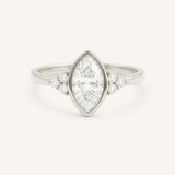 White gold marquise cut bezel set diamond engagement ring with side stones on white background