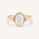 Rose gold oval cut bezel set diamond engagement ring with side stones on white background