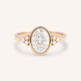 Rose gold oval cut bezel set diamond engagement ring with side stones on white background