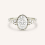White gold oval cut bezel set diamond engagement ring with side stones on white background