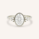 White gold oval cut bezel set diamond engagement ring with side stones on white background