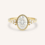 Yellow gold oval cut bezel set diamond engagement ring with side stones on white background