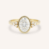 Yellow gold oval cut bezel set diamond engagement ring with side stones on white background