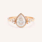 Rose gold pear cut bezel set diamond engagement ring with side stones on white background