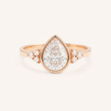 Rose gold pear cut bezel set diamond engagement ring with side stones on white background