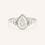 White gold pear cut bezel set diamond engagement ring with side stones on white background
