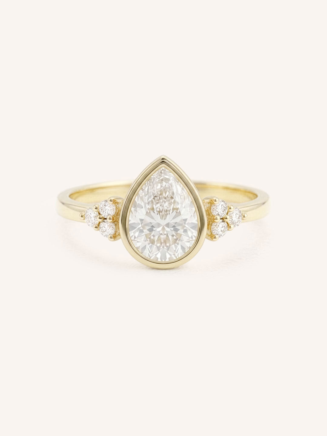 Yellow gold pear cut bezel set diamond engagement ring with side stones on white background