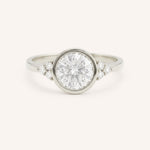 White gold round cut bezel set diamond engagement ring with side stones on white background