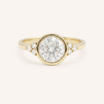 Yellow gold round cut bezel set diamond engagement ring with side stones on white background