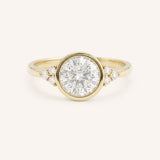Yellow gold round cut bezel set diamond engagement ring with side stones on white background