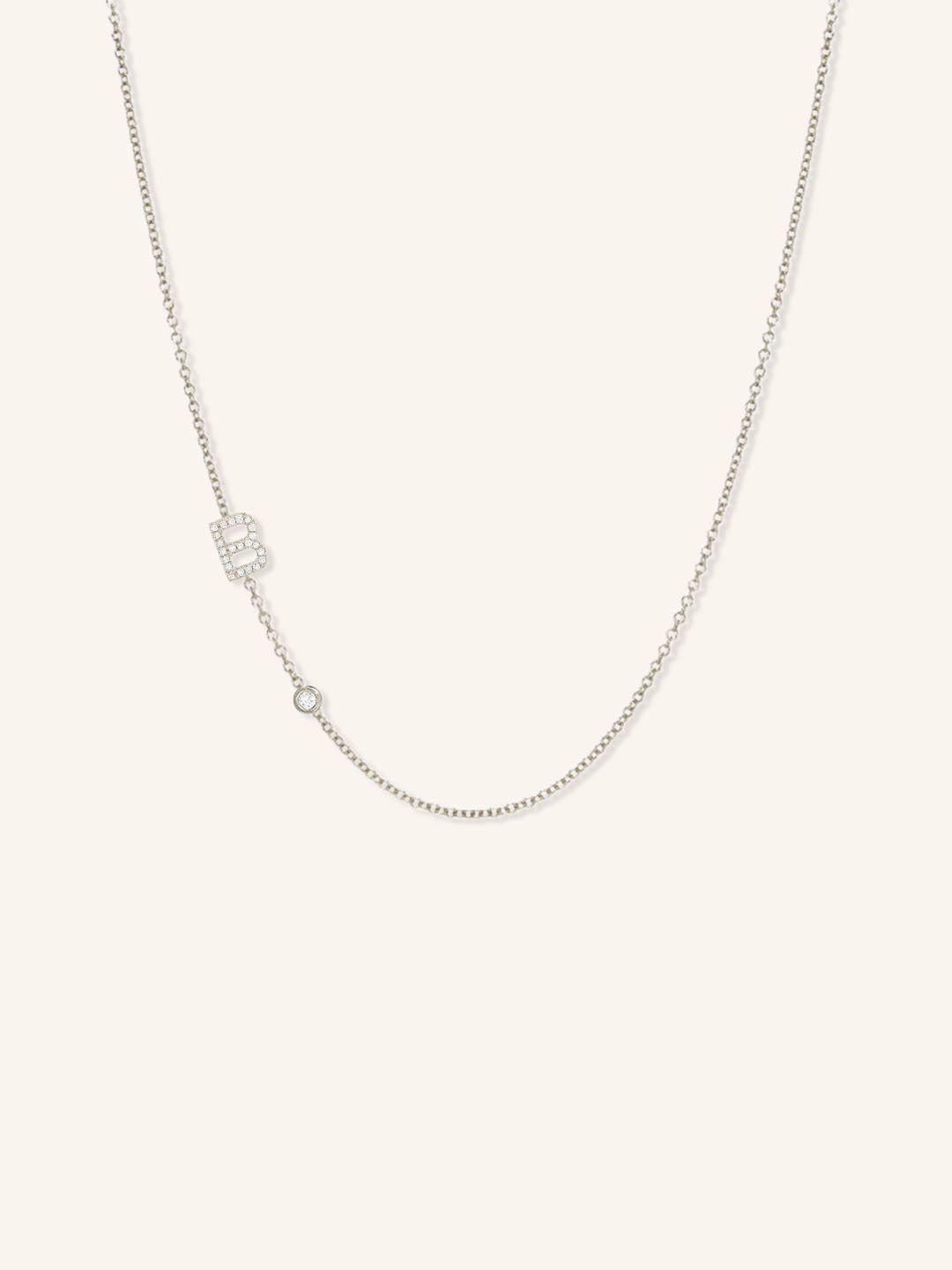 White gold asymmetrical diamond initial B and bezel necklace on white background