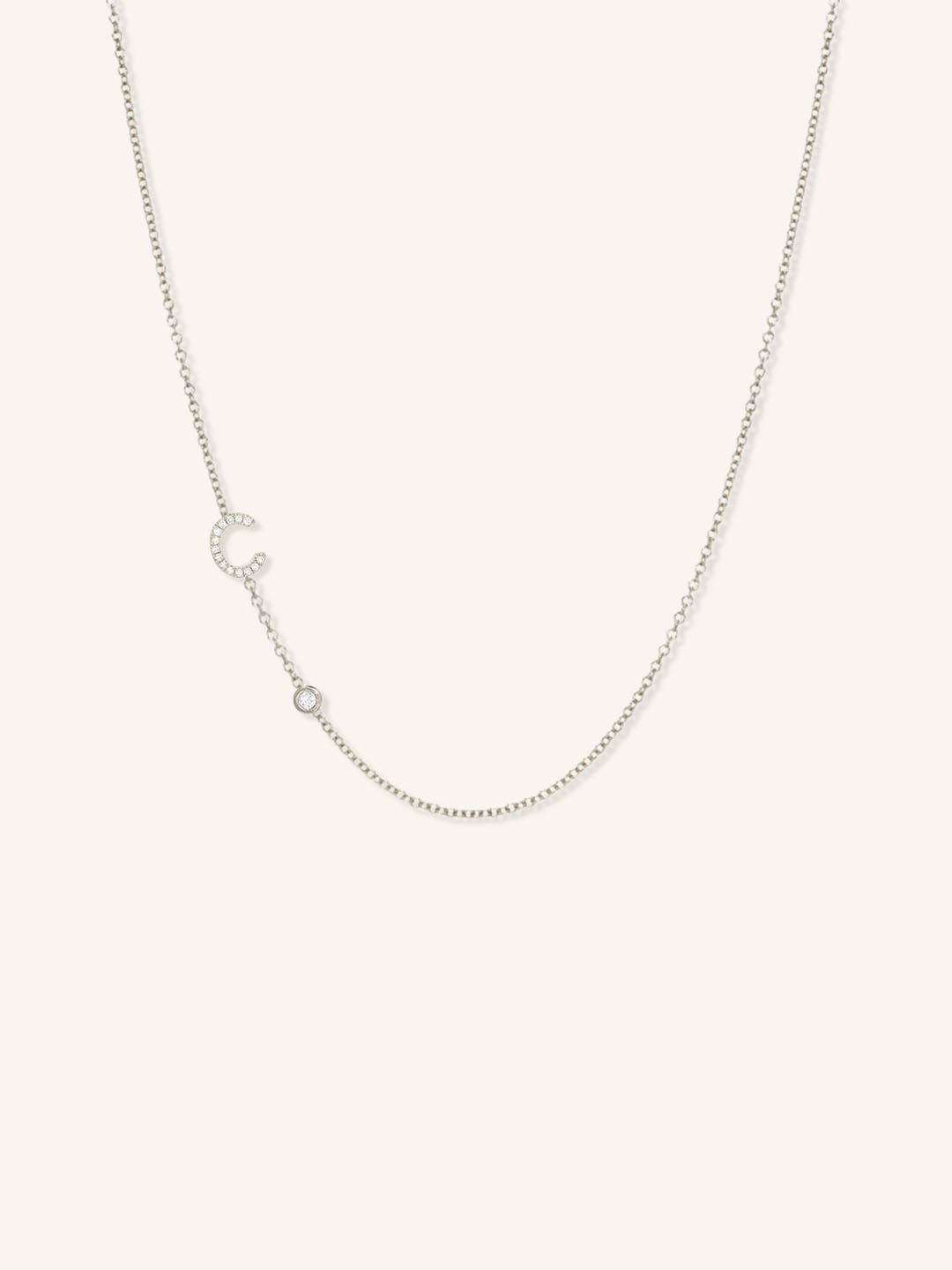 White gold asymmetrical diamond initial C and bezel necklace on white background