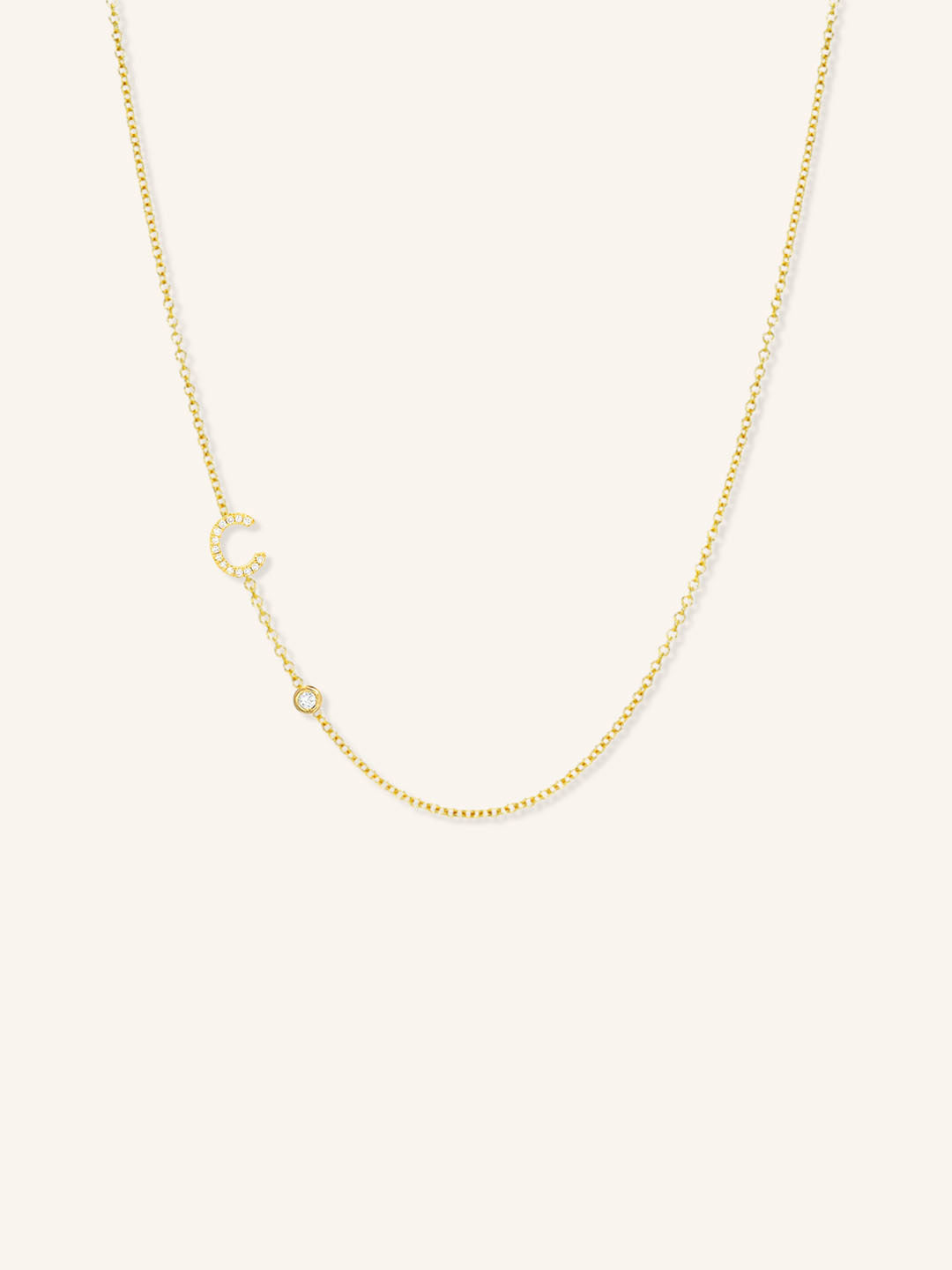 Yellow gold asymmetrical diamond initial C and bezel necklace on white background