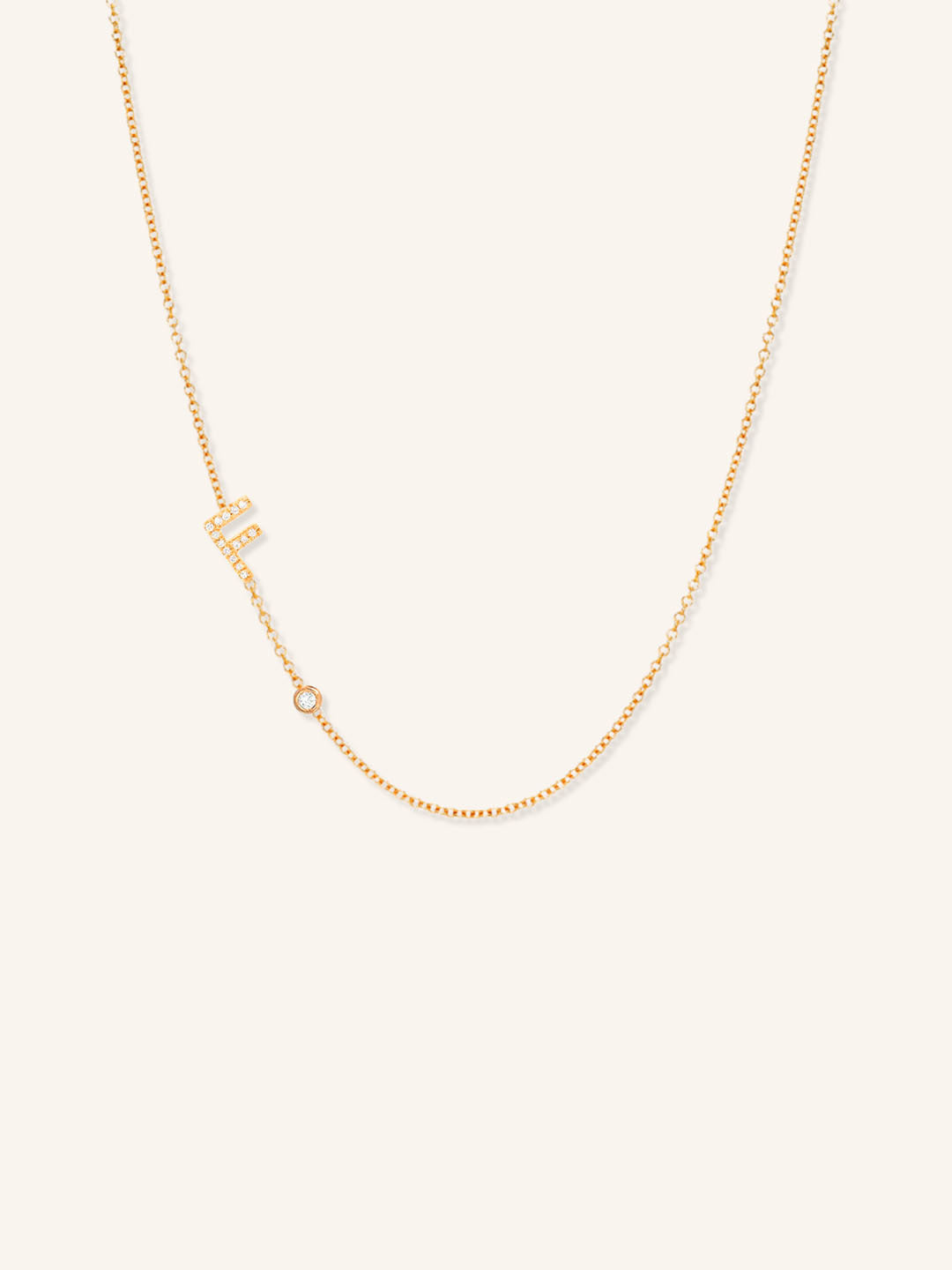 Rose gold asymmetrical diamond initial F and bezel necklace on white background