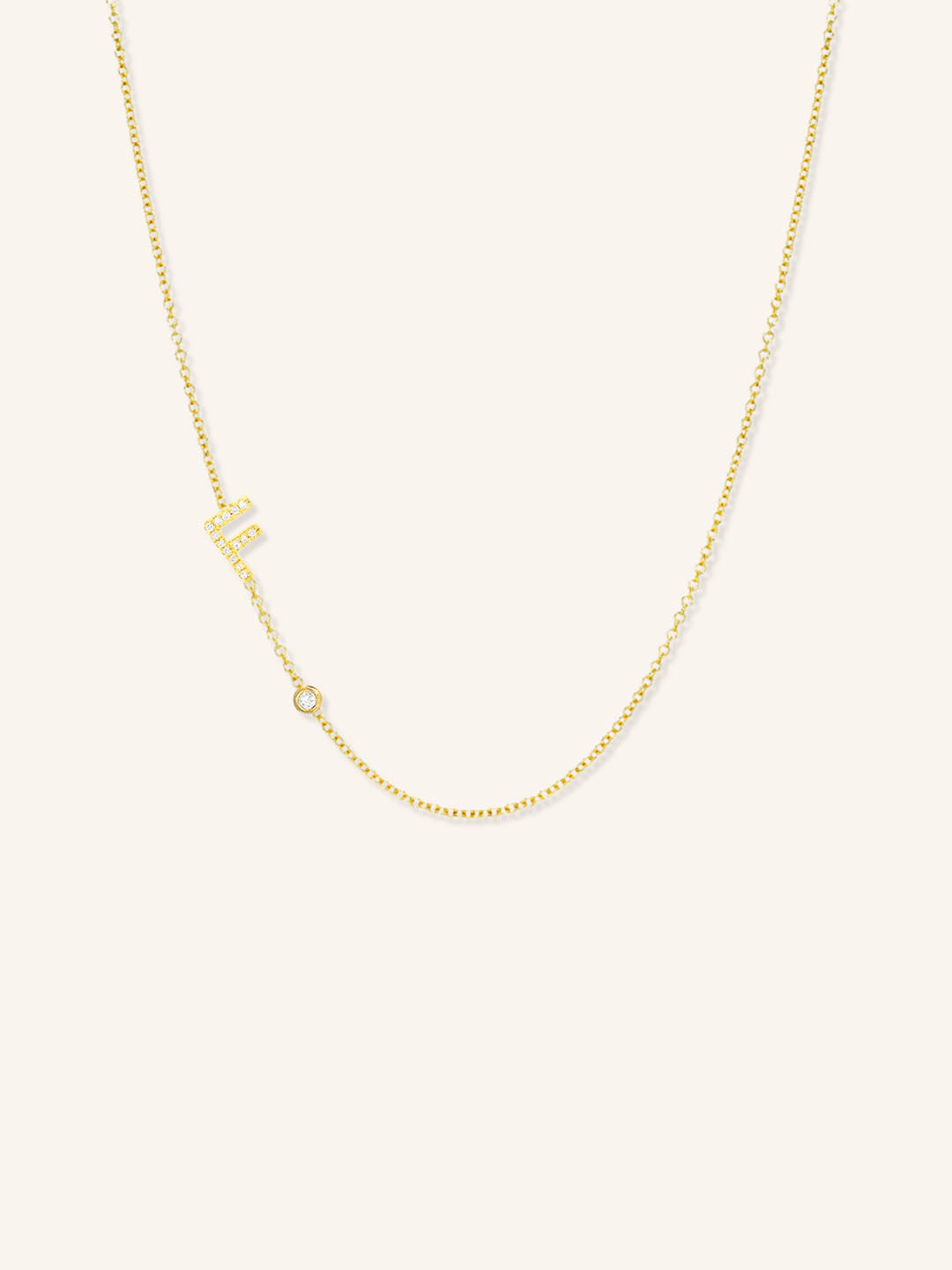 Yellow gold asymmetrical diamond initial F and bezel necklace on white background