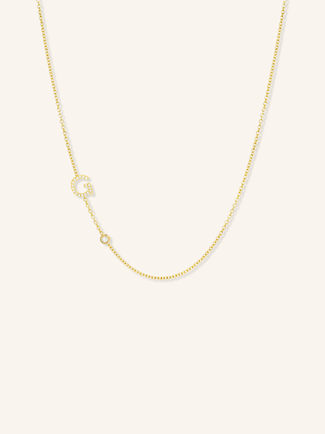 Yellow gold asymmetrical diamond initial G and bezel necklace on white background