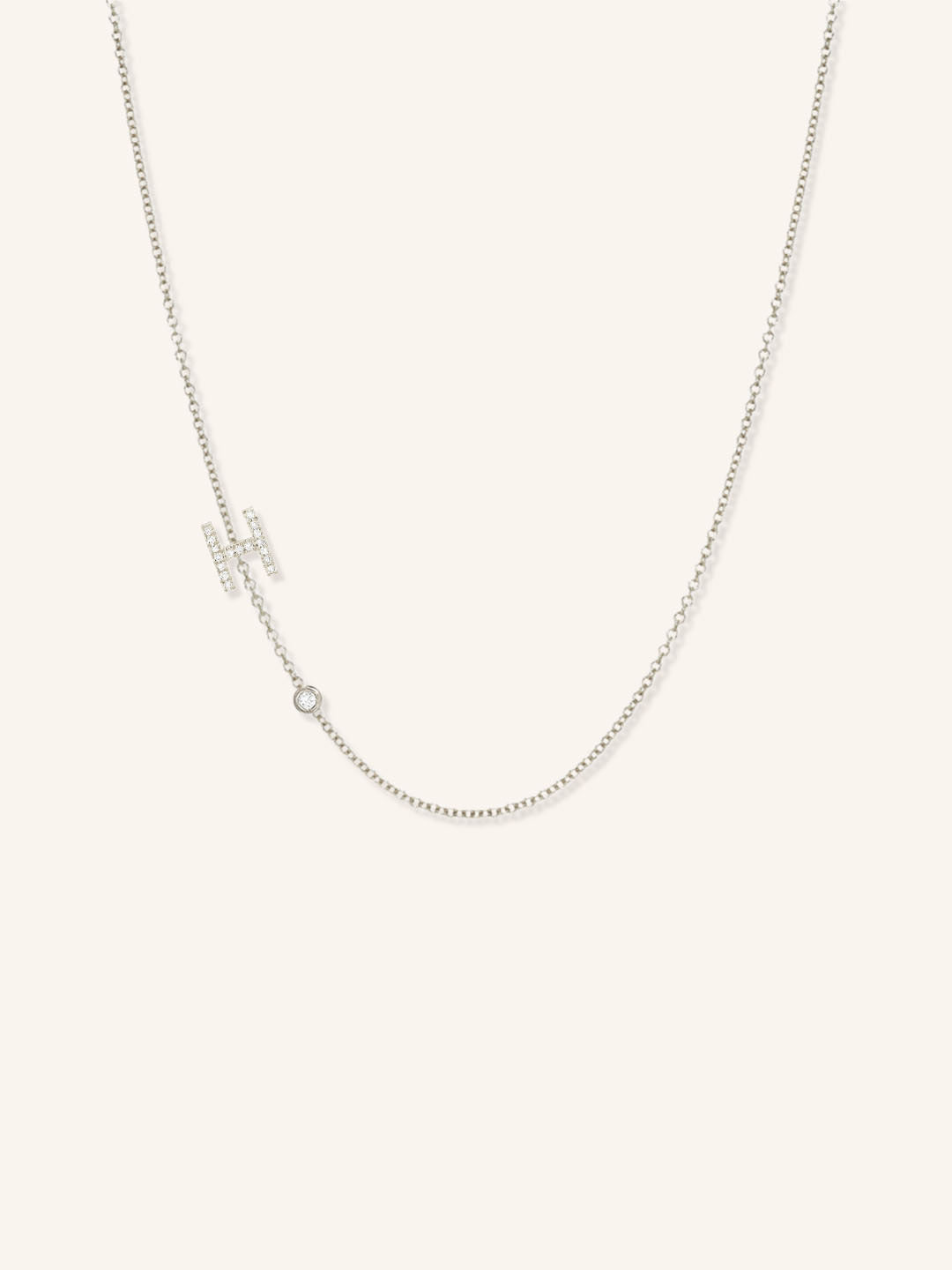 White gold asymmetrical diamond initial H and bezel necklace on white background