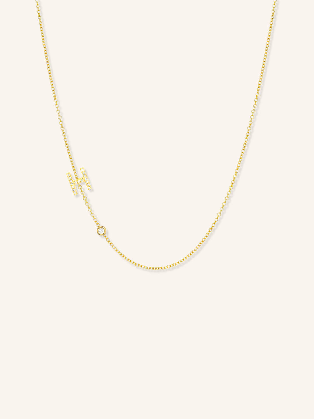 Yellow gold asymmetrical diamond initial H and bezel necklace on white background