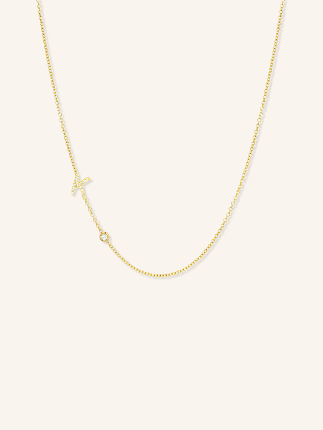 Yellow gold asymmetrical diamond initial K and bezel necklace on white background