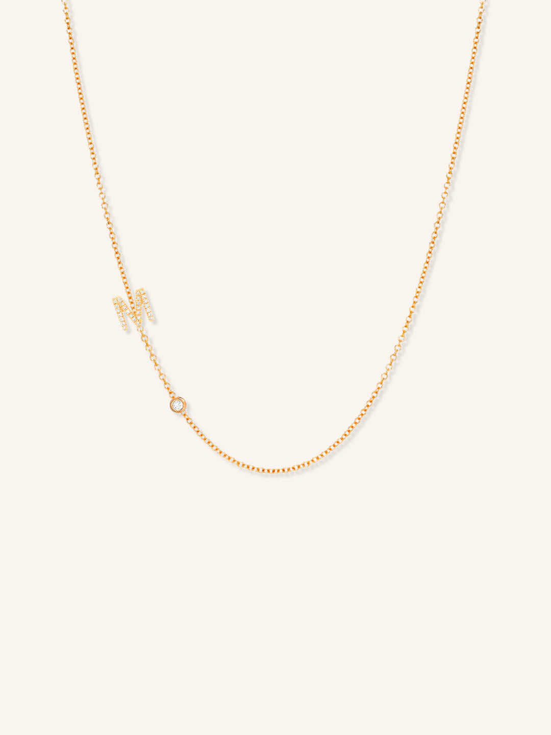 Rose gold asymmetrical diamond initial M and bezel necklace on white background