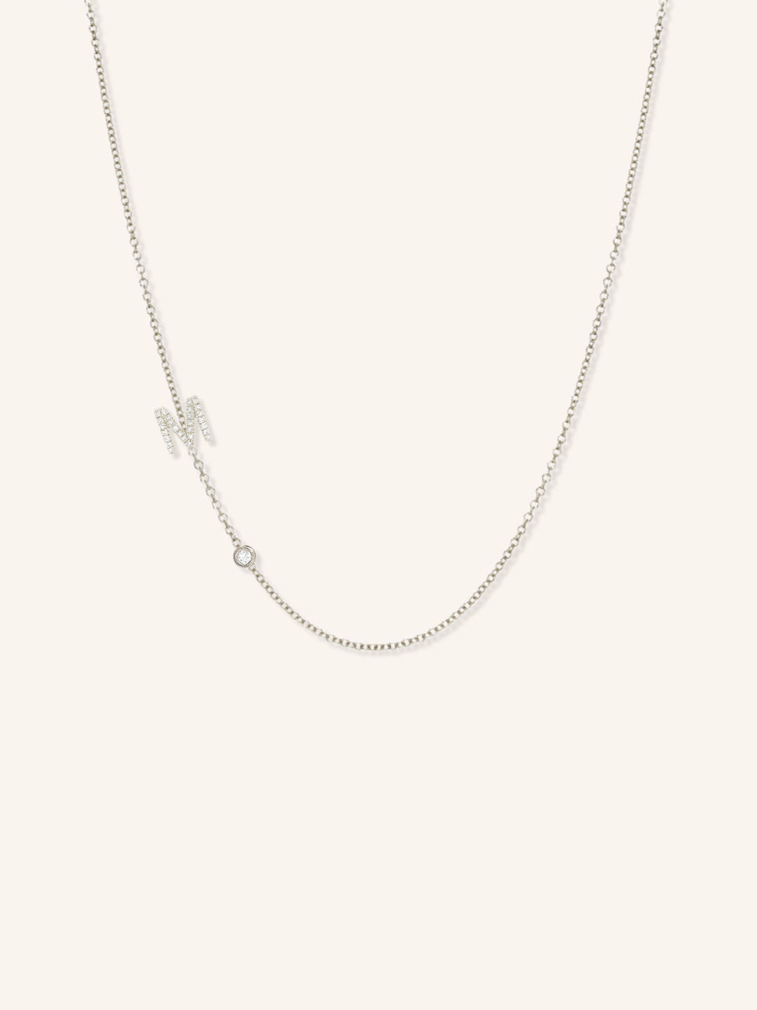 White gold asymmetrical diamond initial M and bezel necklace on white background