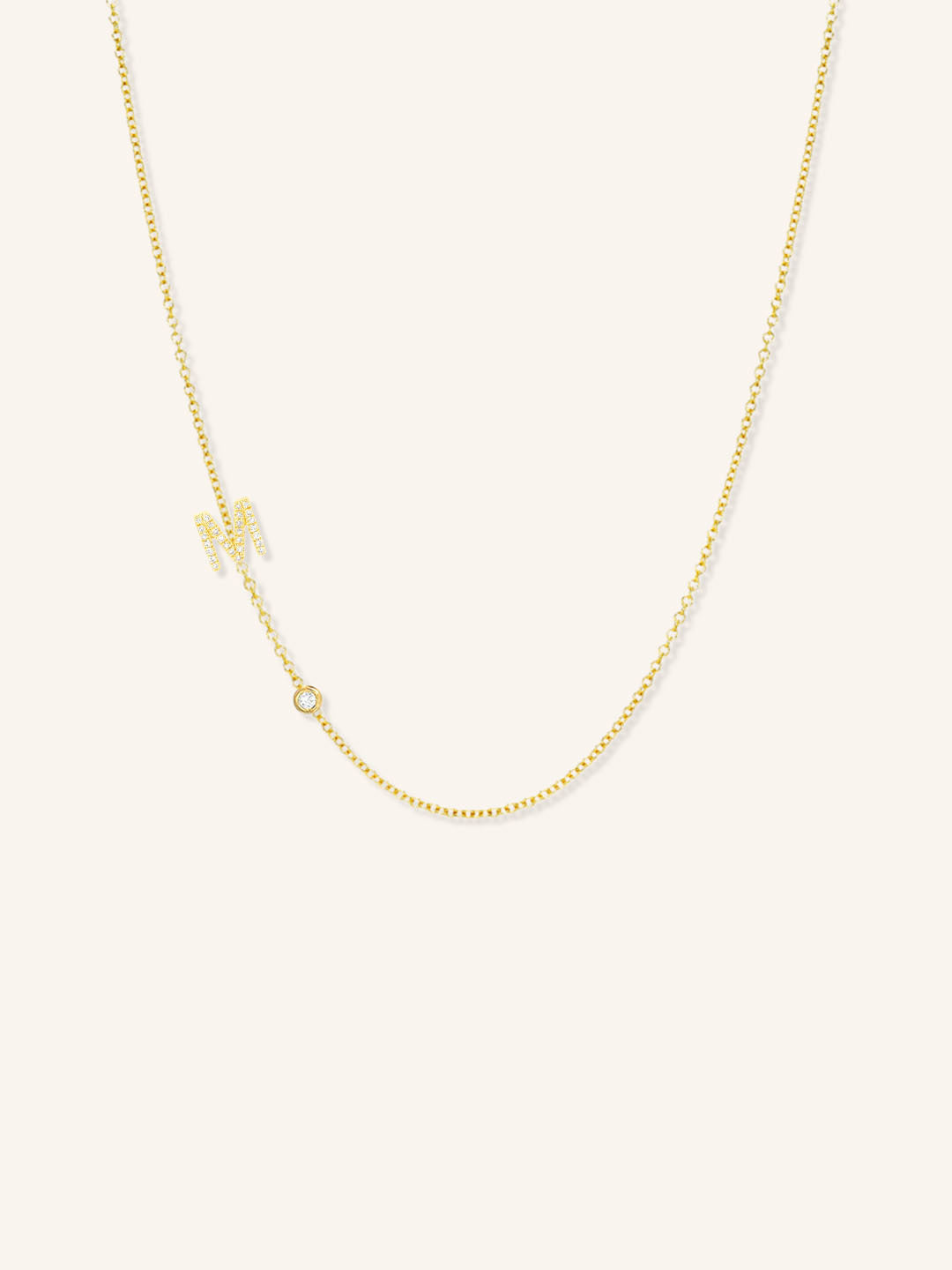 Yellow gold asymmetrical diamond initial M and bezel necklace on white background