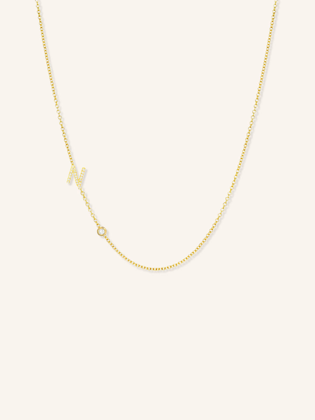 Yellow gold asymmetrical diamond initial N and bezel necklace on white background