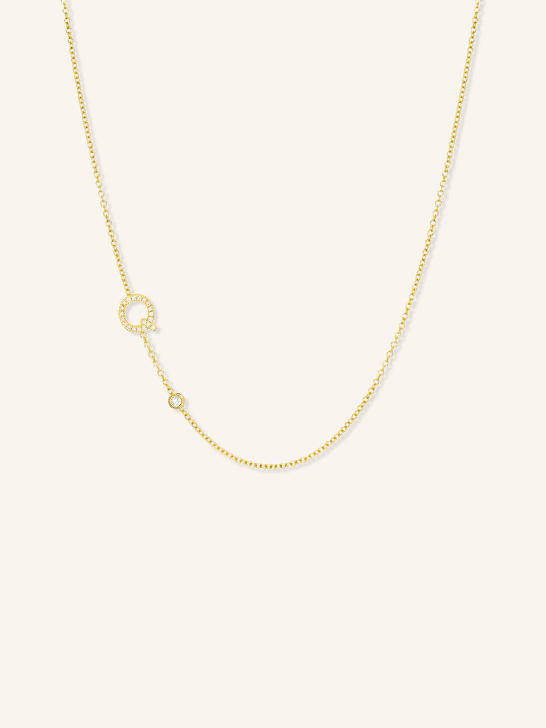 Yellow gold asymmetrical diamond initial Q and bezel necklace on white background