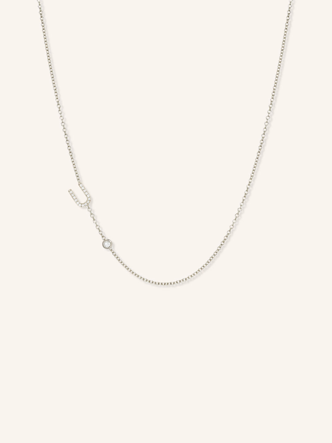 White gold asymmetrical diamond initial U and bezel necklace on white background