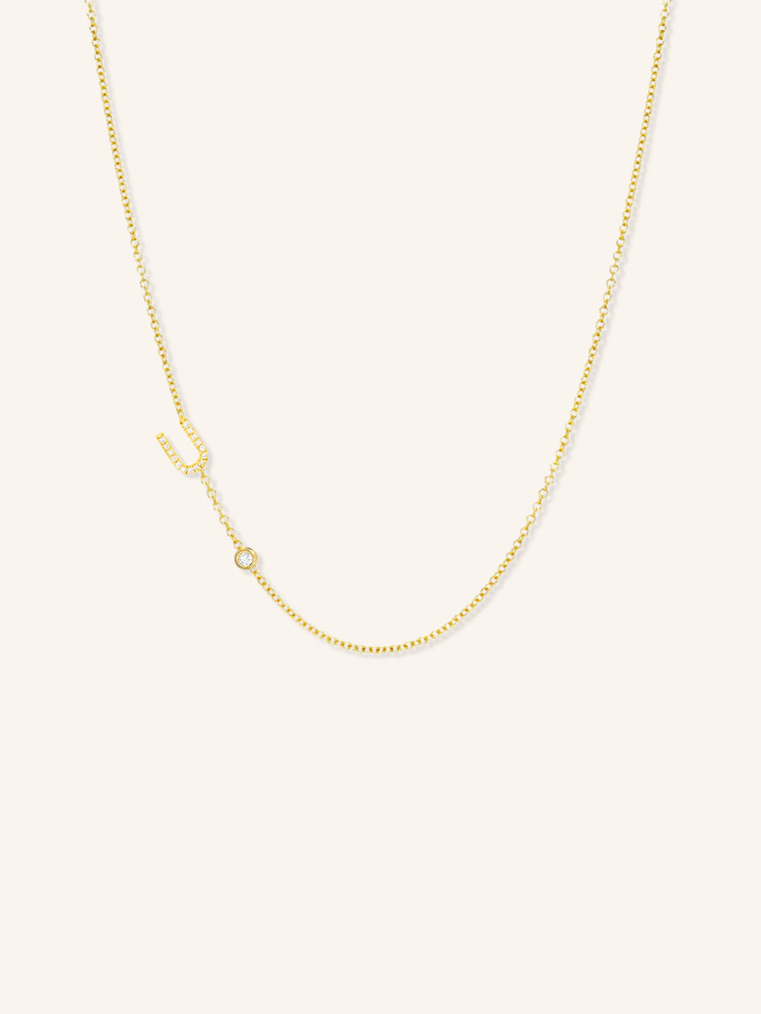 Yellow gold asymmetrical diamond initial U and bezel necklace on white background