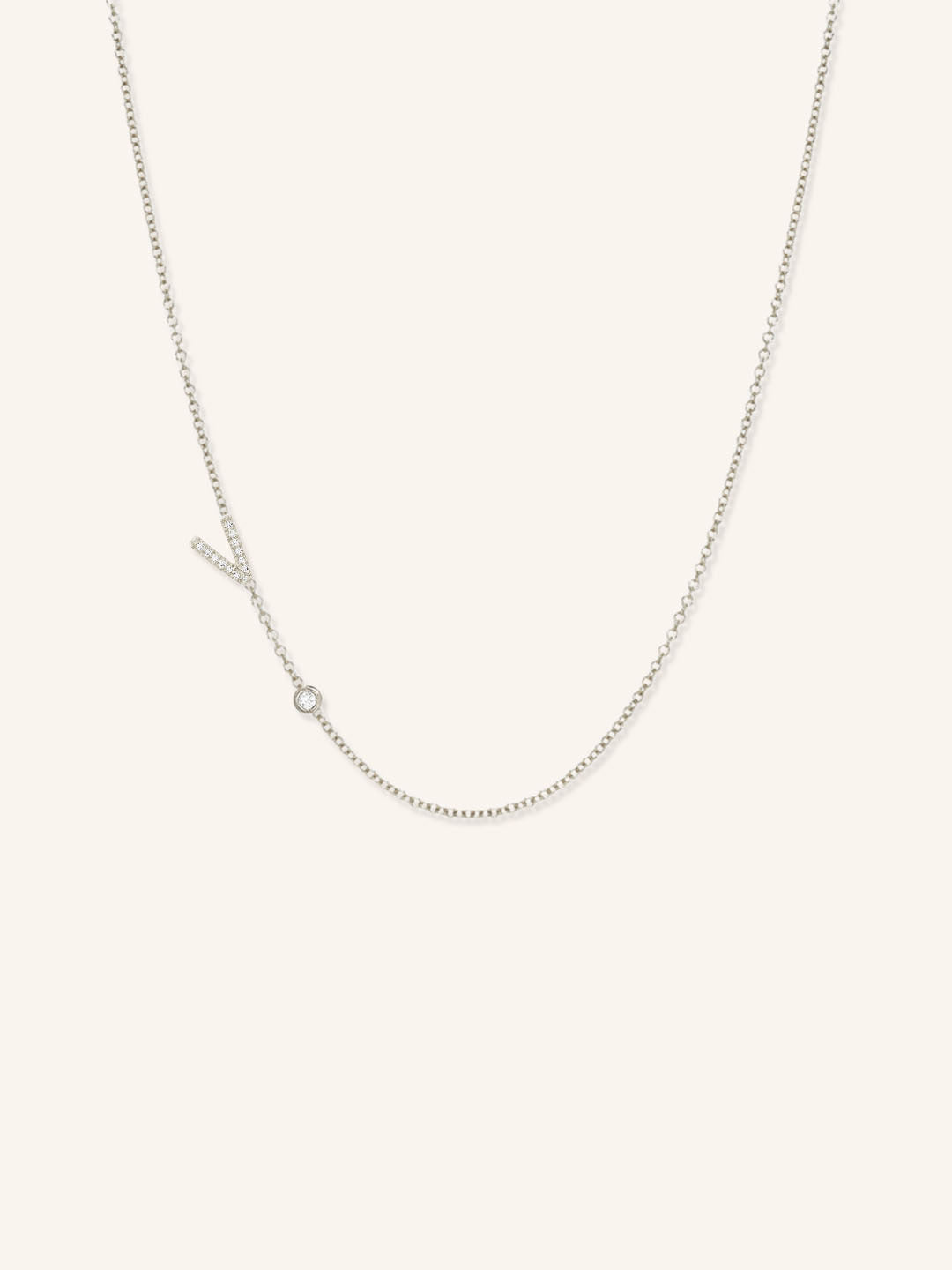 White gold asymmetrical diamond initial V and bezel necklace on white background