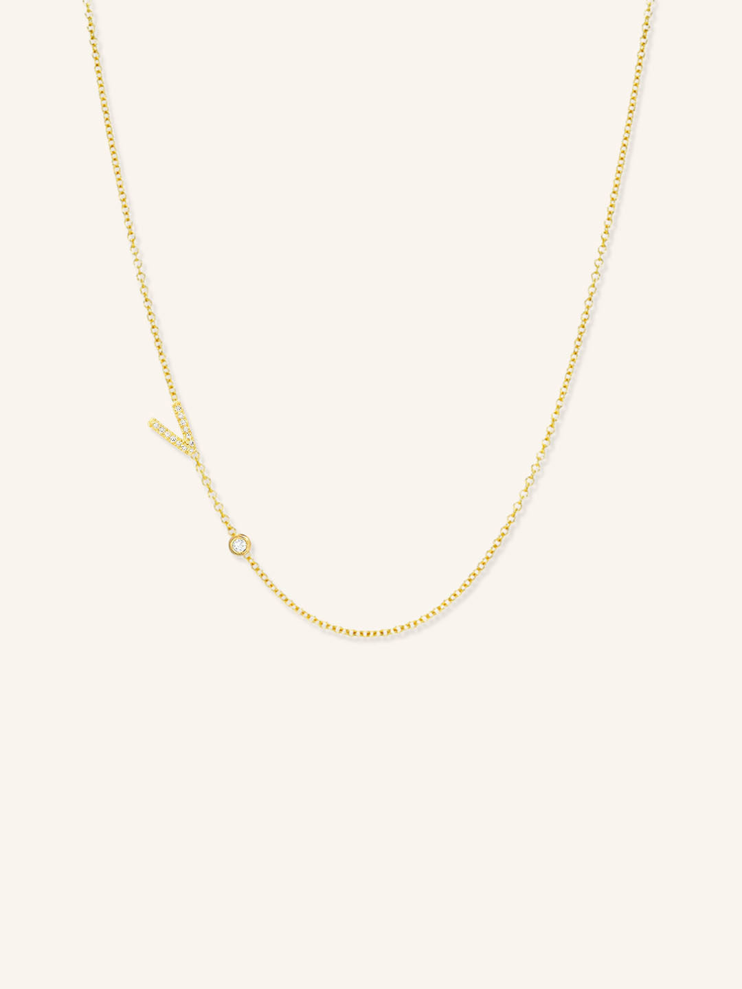 Yellow gold asymmetrical diamond initial V and bezel necklace on white background