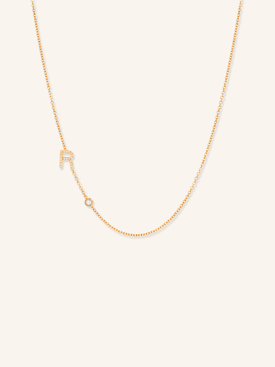 Rose gold asymmetrical diamond initial R and bezel necklace on white background