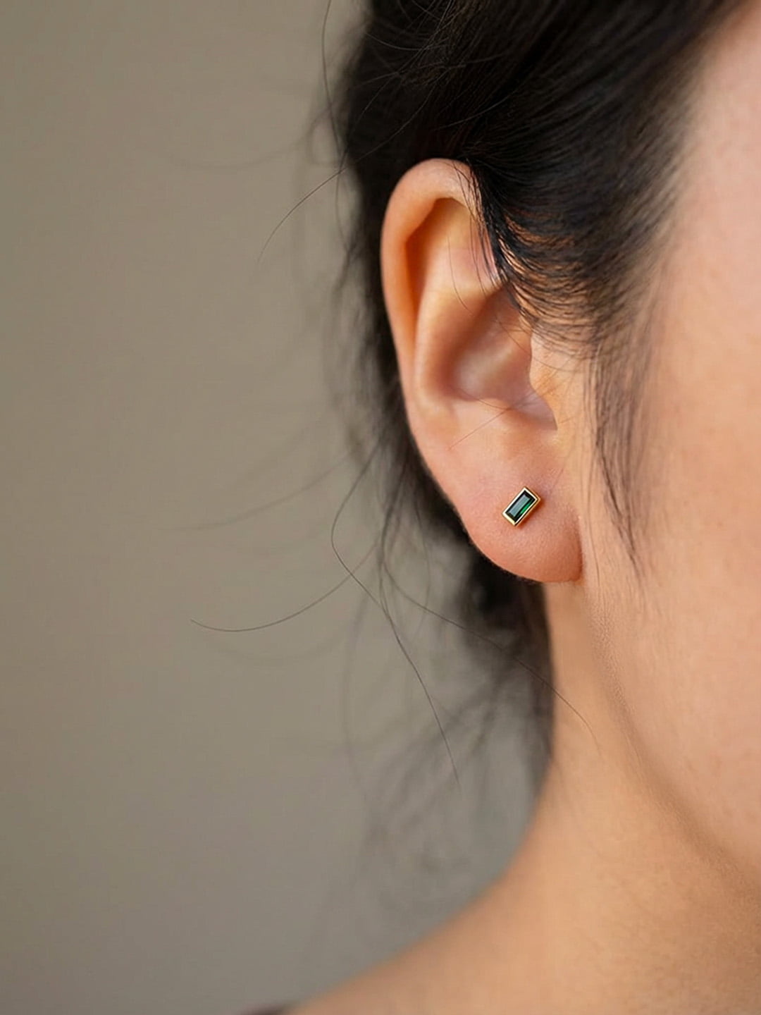 Close-up of an ear wearing a small green earring against a neutral background